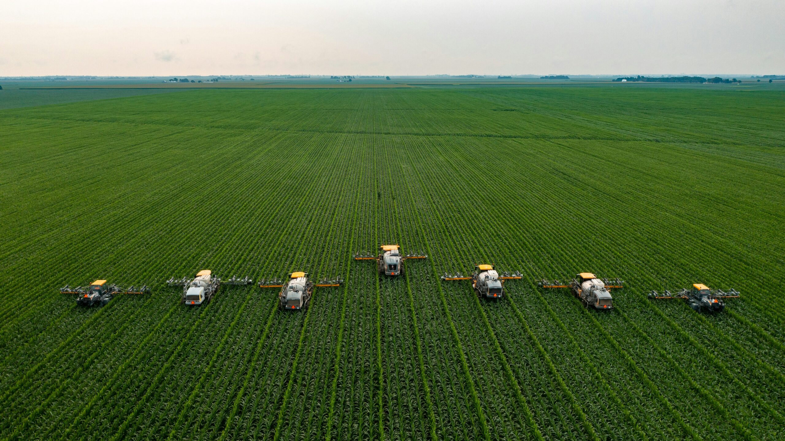 Aerial view of tractors spraying a green crop field
